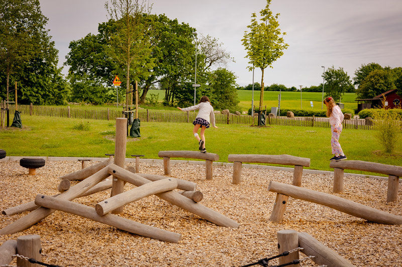 Two girls walking on wooden logs in a playground